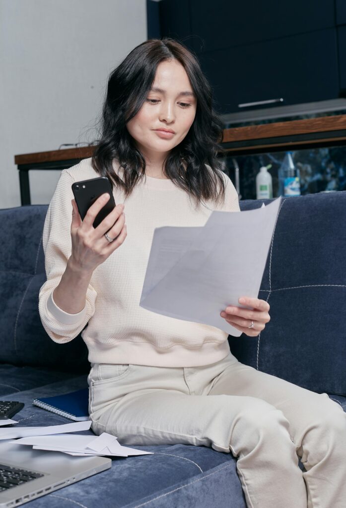 Young woman using phone and documents for home finance management.